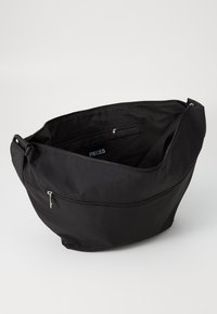 Saco de tecido preto com uma abertura ampla, apresentando um fecho de zipper, bolsos interiores e um discreto rótulo "PIECES". Textura suave.