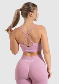 Sostenedor deportivo de color rosa claro con tirantes entrelazados, combinado con leggings de tiro alto. Textura suave, con una marca mínima en la cinturilla.