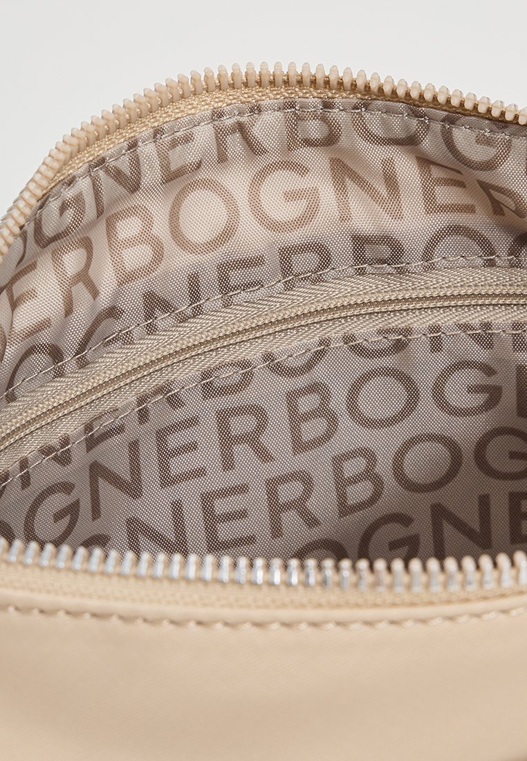 Beige Reisetasche mit glatter Außenseite. Das Innere weist ein sich wiederholendes Logo-Muster in warmen Farben auf. Der Reißverschluss hat eine silberne Beschichtung.