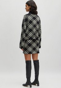 Schwarzer und cremefarbener kariertes Strickpullover mit einem cropped Design, kombiniert mit einem passenden Rock. Das Model trägt kniehohe schwarze Lederstiefel.