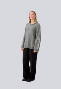 Gray knitted sweater with a relaxed fit, featuring a ribbed neckline and contrasting textured pattern along the sleeves. Paired with black trousers.