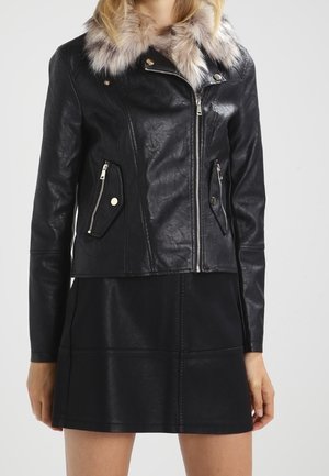 Zwart leren jack met bontkraag en zilveren ritsen, gedragen over een zwarte leren rok, weergegeven van halverwege de schouder tot halverwege de dij.