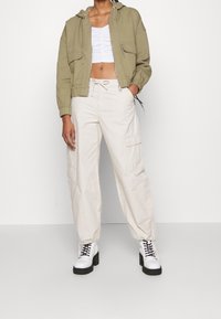 Felpa con cappuccio verde oliva tagliata, con tasche frontali, abbinata a pantaloni cargo beige con tasche laterali. Stivaletti bianchi chunky con lacci completano il look.