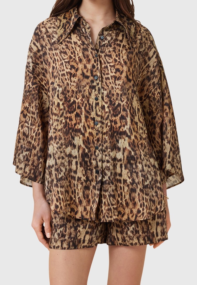 Chemise imprimé léopard à coupe oversized, manches courtes et fermeture par boutons. Confectionnée en tissu léger avec boutons noirs et assortie à un short.