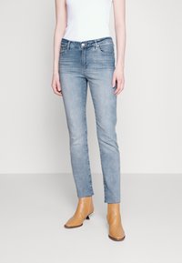 Jeans de denim azul claro con un corte ajustado, talle medio, cinco bolsillos y un desvanecimiento sutil. Combinados con botas de tobillo color beige.