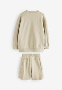 Sudadera beige con cuello redondo y mangas largas, combinada con pantalones cortos a juego que cuentan con una cintura elástica y un bolsillo lateral.