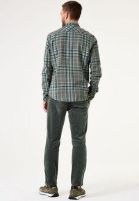 Grijs geblokt overhemd met groene en blauwe accenten, gecombineerd met donkergroene corduroy broek en casual sneakers met een witte zool.