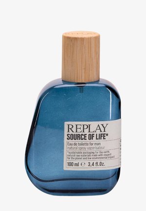 Blå glasflaske med en uregelmæssig form, træprop og en hvid etiket med sort tekst. Indeholder 100 ml eau de toilette.