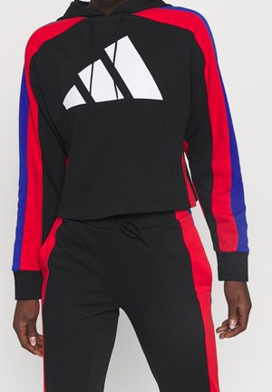 Completo con felpa nera con cappuccio e pantaloni, con strisce rosse e blu sulle maniche e sui pantaloni, caratterizzato da un grande logo grafico bianco sul petto.