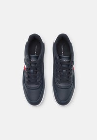 Sneaker in pelle blu navy con suole in gomma bianca. Le caratteristiche includono dettagli perforati, design con lacci e una striscia di accento rossa e bianca.