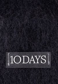 Zwart fuzzy stof met een rechthoekige patch met "10 DAGEN" in witte hoofdletters.