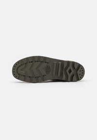 Suela de zapato en goma de color gris oscuro con un patrón texturizado, que presenta ranuras profundas para tracción y orificios de ventilación a lo largo de los bordes.