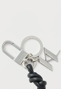 Silver keychain featuring a carabiner clip, a round ring with "KARL LAGERFELD," and two metal accents, one rectangular and one triangular, on a black leather cord.