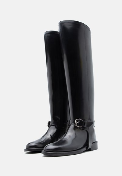 Cizme din piele neagră, până la genunchi, cu finisaj lucios, prevăzute cu o curea cu cataramă și design cu vârf rotund. Textură netedă și talpă solidă.