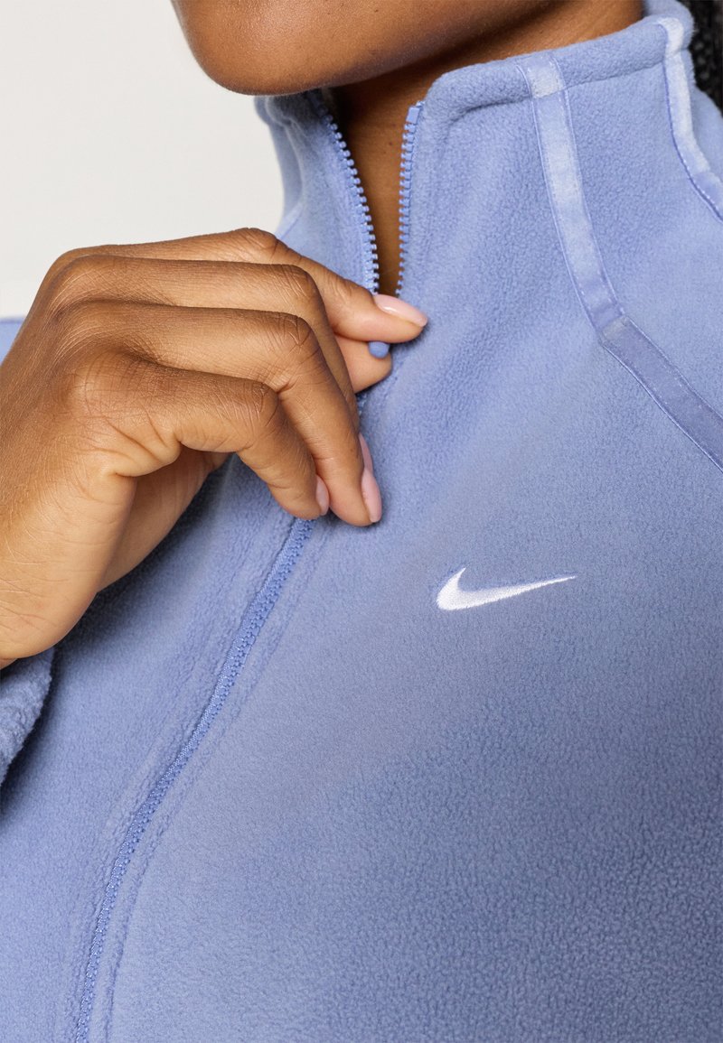 Helles, blaues Fleece-Jacke mit einem Reißverschluss-Kragen, versehen mit einem weißen Nike-Logo auf der Brust und einer glatten, weichen Textur.