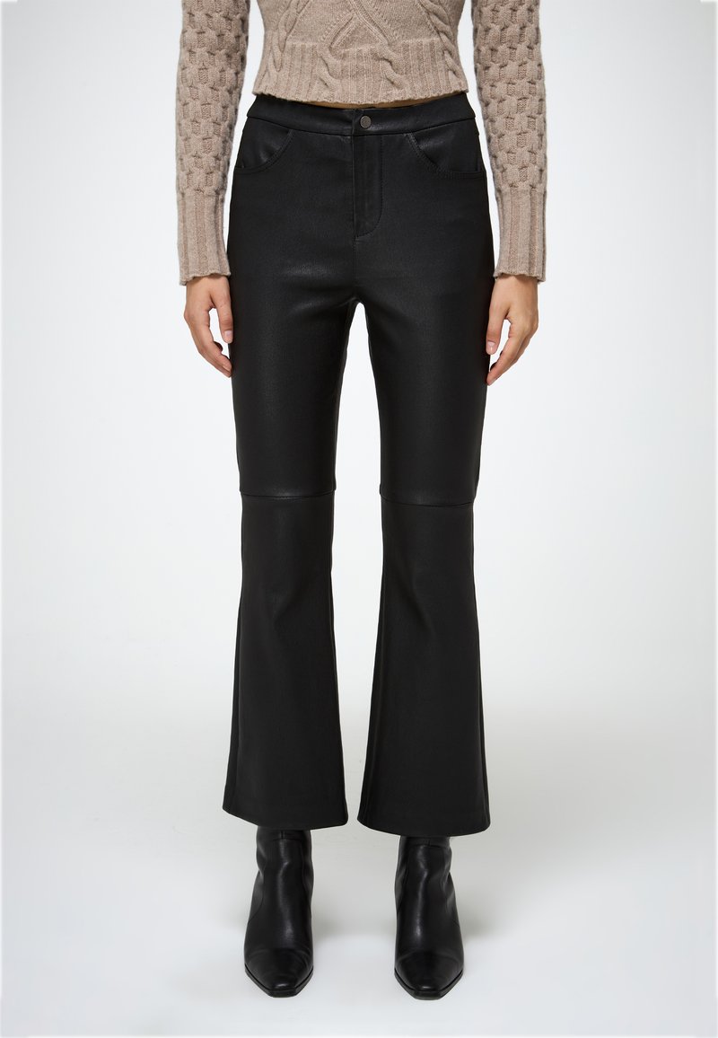 Pantalones de campana negros con una textura lisa y suave, que cuentan con bolsillos frontales y una cinturilla con cierre de botón. Combinados con botas de tacón negras.