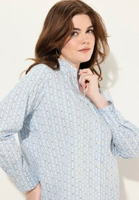 Camisa abotonada con cuello alto, con un fondo azul claro y rayas verticales en púrpura y turquesa, con acentos florales.