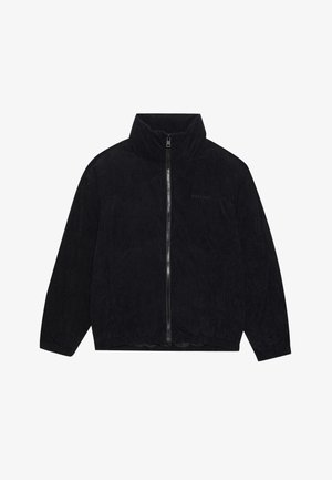 Chaqueta de pana negra con cremallera y cuello alto, textura acanalada y dobladillo elástico. Presenta una sutil marca en el pecho.