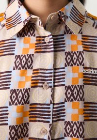 Kortärmad skjorta med knappar och ett flerfärgat geometriskt mönster, som har orange, blå och bruna nyanser, tillverkad av lättvikts tyg.