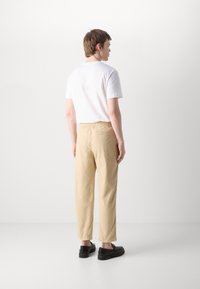 Beige elastiske bukser med rett snitt og strikk i livet, kombinert med en enkel hvit t-skjorte og svarte sko. Stoffet ser jevnt og lett ut.