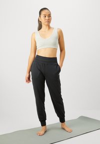 Gray sports bra and black jogger pants, both featuring a smooth texture and elastic waistband, displayed on a light yoga mat.