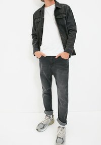 Giacca di denim nera sopra una maglietta bianca, abbinata a jeans grigi e sneakers grigi. Texture liscia, orli arrotolati sui jeans, vestibilità casual.
