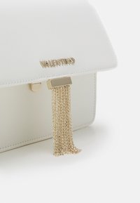 Vit läderhandväska med en guldkedja tassel detaljer, som har en geometrisk klaffstängning och präglad varumärkesbokstäver på framsidan.