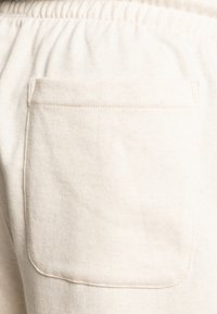Sweatpants in cream cotton with a soft texture, featuring an attached back pocket with a visible seam detail for added utility.