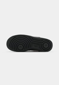 Suela de zapatilla negra con patrones circulares, superficie texturizada y áreas de acento ligeramente elevadas. Material de goma con surcos profundos para tracción.