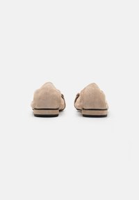 Beige semskede loafers med lav profil, rund tå og gummisåle. Har en glat tekstur med minimal sømdetalj.