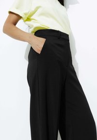 Pantalons noirs à jambes larges avec une texture lisse et des poches latérales, associés à un haut à manches courtes de couleur jaune clair. Design simple et moderne.