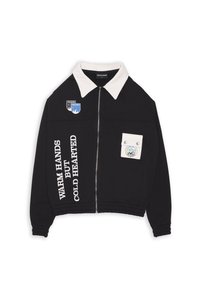 Giacca nera con zip frontale e colletto bianco, caratterizzata da testo stampato sulle maniche e toppe sulla tasca del petto, realizzata in tessuto morbido.