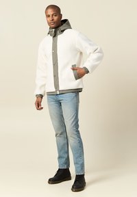 Biała polarowa kurtka z szarym wykończeniem, z zapięciem na guziki i kapturem; w połączeniu z jasnoniebieskimi dżinsami i czarnymi laced-up botkami.