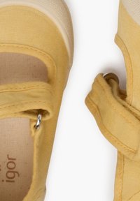 Scarpe di tela gialle con punta arrotondata e suola in gomma. Presentano una fascia in Velcro e dettagli di cucitura visibili.