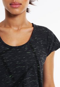 Zwart getextureerd T-shirt met korte mouwen, voorzien van een losse halslijn en dunne groene gespikkelde patronen over de hele stof.