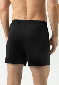 Les boxers noirs sont confectionnés dans un tissu doux, dotés d'une ceinture élastique et d'un design simple et sans coutures. La vue arrière montre une texture lisse.