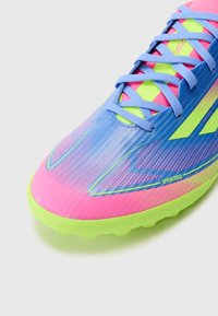 Helle pinke und blaue Fußballschuhe mit strukturierter synthetischer Oberseite, grünen Akzenten und einem gerippten Design. Verfügt über ein ausgeklügeltes Schnürsystem und ein Logo.