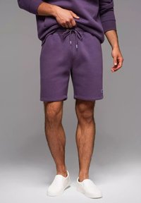 Lila Baumwollshorts mit einem elastischen Bund und Kordelzug. Verfügt über Seitentaschen und einen Logopatch am unteren linken Saum. Weiße Slipschuhe.