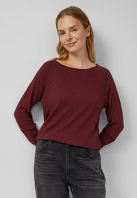 Burgundia pikkade varrukatega pluus, millel on avar kaelus, valmistatud pehmest kangast; kombineeritud tumehallide teksadega, millel on mugav lõige.