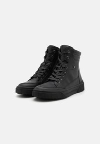 Svarte høyhælte sneakers laget av lær, med runde tær, snøring, polstret krage og teksturerte gummisåler med riller.