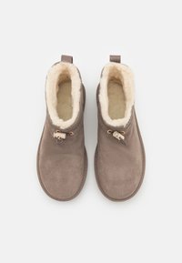 Paire de chaussons marron en daim à enfiler avec doublure en peluche de couleur crème et fermetures à cordon réglables, vus de dessus sur fond blanc.