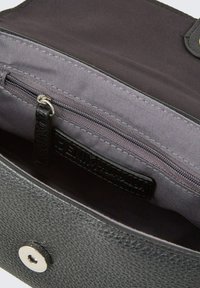 Interno di una borsa in pelle nera con fodera in tessuto grigio. Caratterizzata da una tasca con zip e un'etichetta marchiata. Chiusura a pressione magnetica visibile.