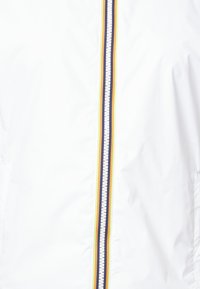 Giacca bianca con una cerniera centrale, caratterizzata da strisce multicolori: blu navy, giallo e verde chiaro. Tessuto liscio e leggero.