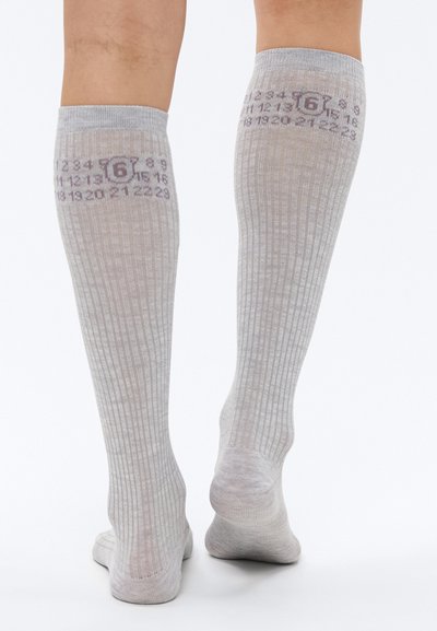 Γκρι κάλτσες μέχρι τα γόνατα με ριμπ υφή, διακοσμημένες με τυπωμένους αριθμούς και ένα μικρό εικονίδιο γύρω από την περιοχή της γάμπας. Απαλό υλικό και χωρίς ραφές σχεδιασμός.