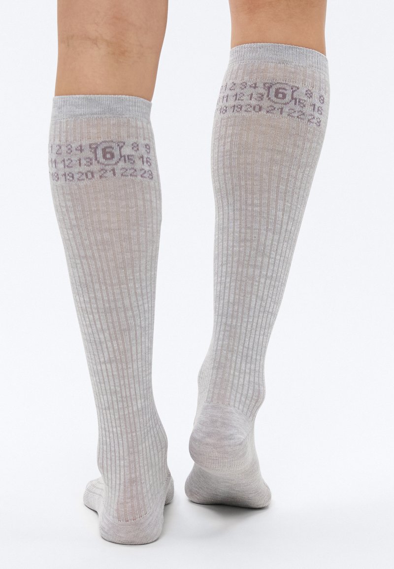 Grå knæstrømper med ribbet tekstur, der har trykte tal og et lille ikon omkring lægområdet. Blødt materiale og sømløst design.