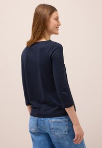 Dunkelblaues Langarmshirt mit Bootsausschnitt und weicher Textur, kombiniert mit hellblauen Jeans aus Denim mit Gesäßtaschen.