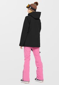 Zwarte waterdichte jas met een capuchon, gecombineerd met roze sneeuwbroeken met ritsen. Versterkt met een kleurrijke beanie en reflecterende goggle.
