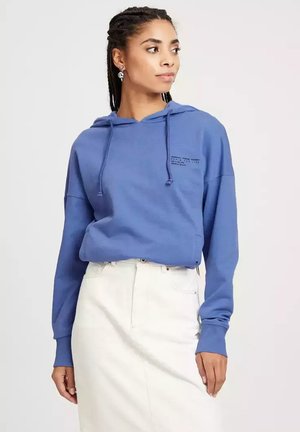 Niebieska bluza z kapturem wykonana z miękkiego materiału, z przednią kieszenią typu kangur, sznurkami do regulacji oraz nadrukowanym tekstem na klatce piersiowej. W zestawie z białą spódnicą.