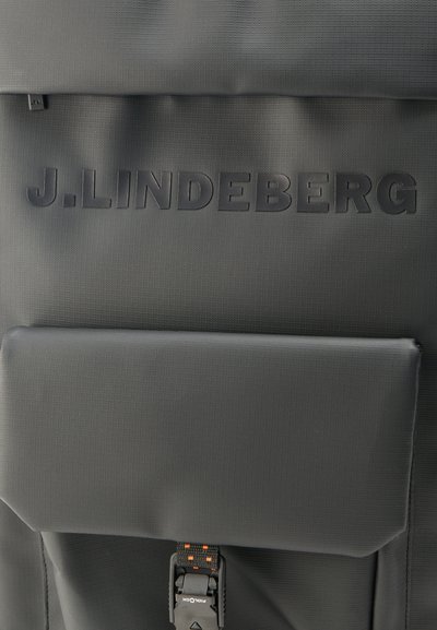 Μαύρο σακίδιο με την ένδειξη «J. LINDEBERG» ανάγλυφη στο καπάκι, με μπροστινή τσέπη που ασφαλίζει με μαύρη αγκράφα με πορτοκαλί λεπτομέρειες.