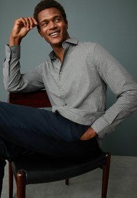 Gray checkered button-up shirt with a collar, worn with dark pants, sitting on a chair, smooth fabric, slim fit, and visible buttons.